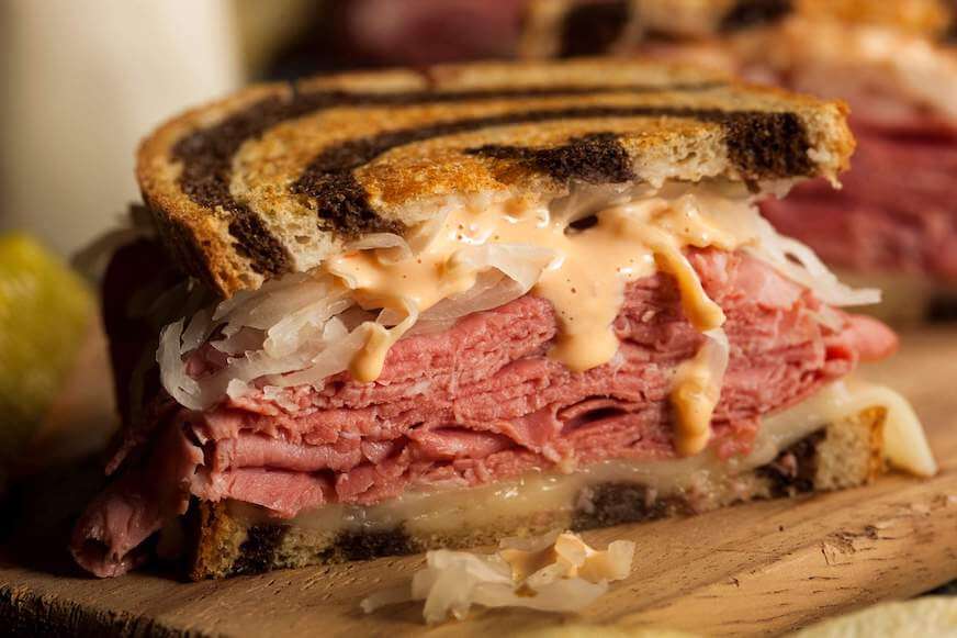 A corned beef sandwich on rye bread with sauerkraut, cheese, and sauce.