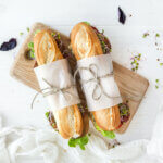 An overhead view of two sub sandwiches wrapped in paper and tied with string on a white tabletop
