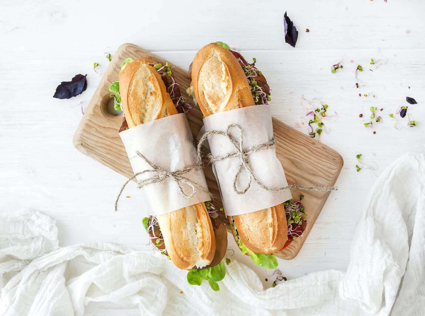 An overhead view of two sub sandwiches wrapped in paper and tied with string on a white tabletop