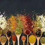 A colorful mix of herbs and spices in wooden spoons and spilling out onto a black background