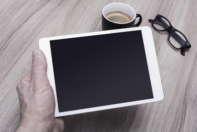 Person holding a tablet next to a cup of coffee.