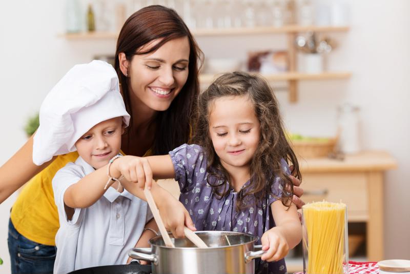 Kids and their mom making pasta in the kitchen.