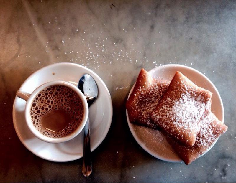 Two beignets topped with powdered sugar rest next to an espresso.