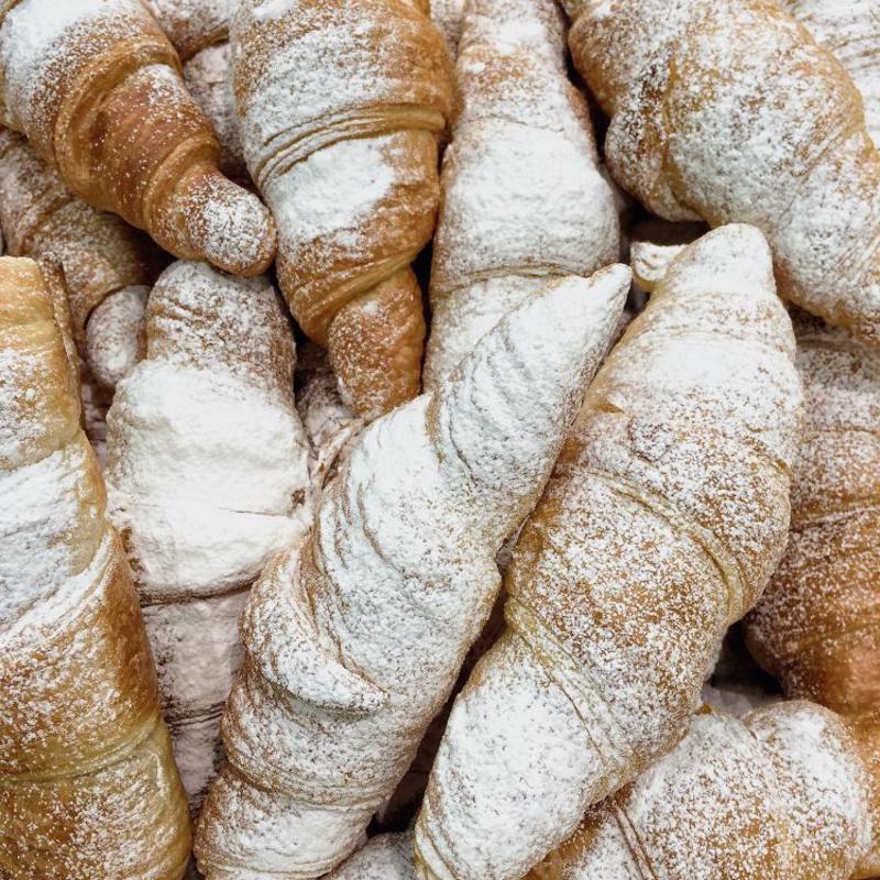 A bowl of croissants dusted with powdered sugar.