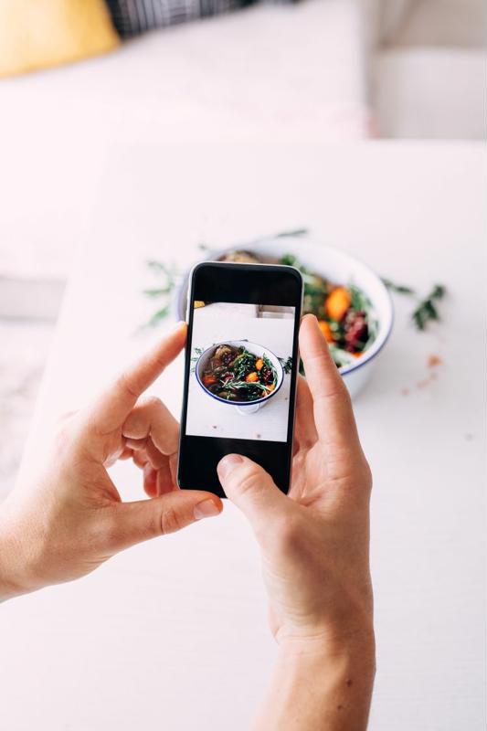 A chef takes a picture of a plated dish with a smartphone.