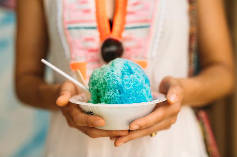 A woman holds a bowl of blue and green brightly colored shaved ice.
