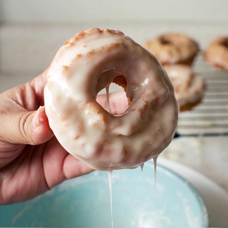 Vanilla glaze drips from a dipped doughnut.