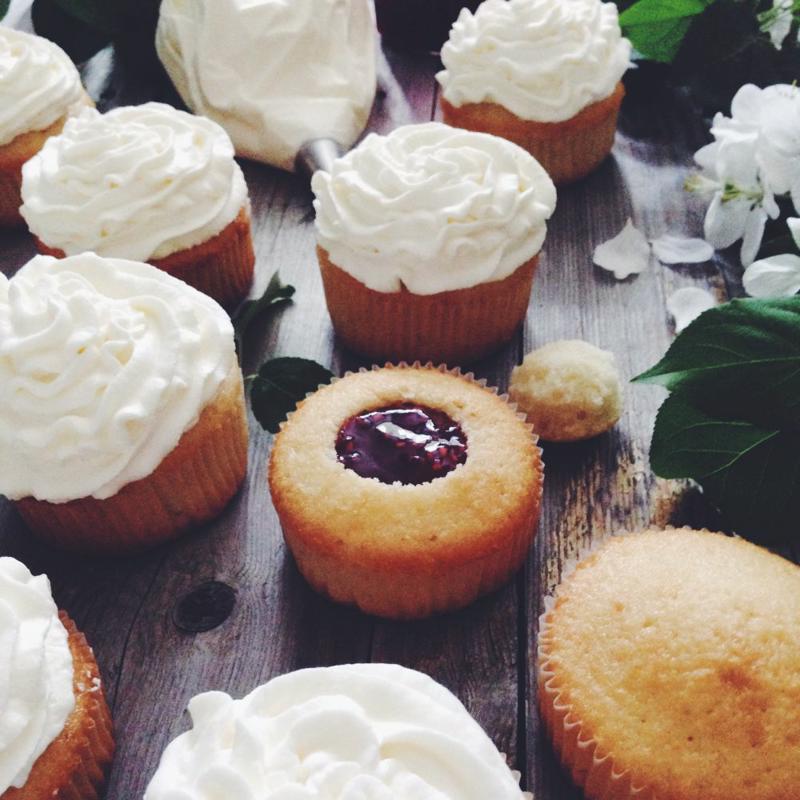 Cupcakes in various stages of completion on a wooden table.